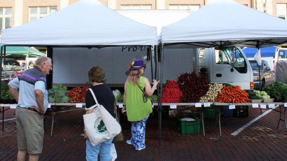 Shoppers buy vegetables at a farmers market.