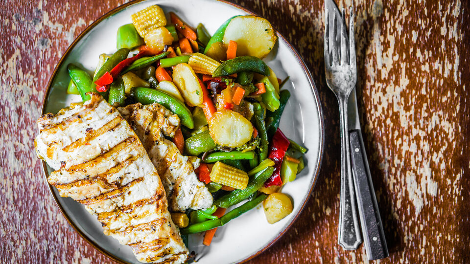 Grilled chicken and vegetables on a plate on a rustic tabletop.