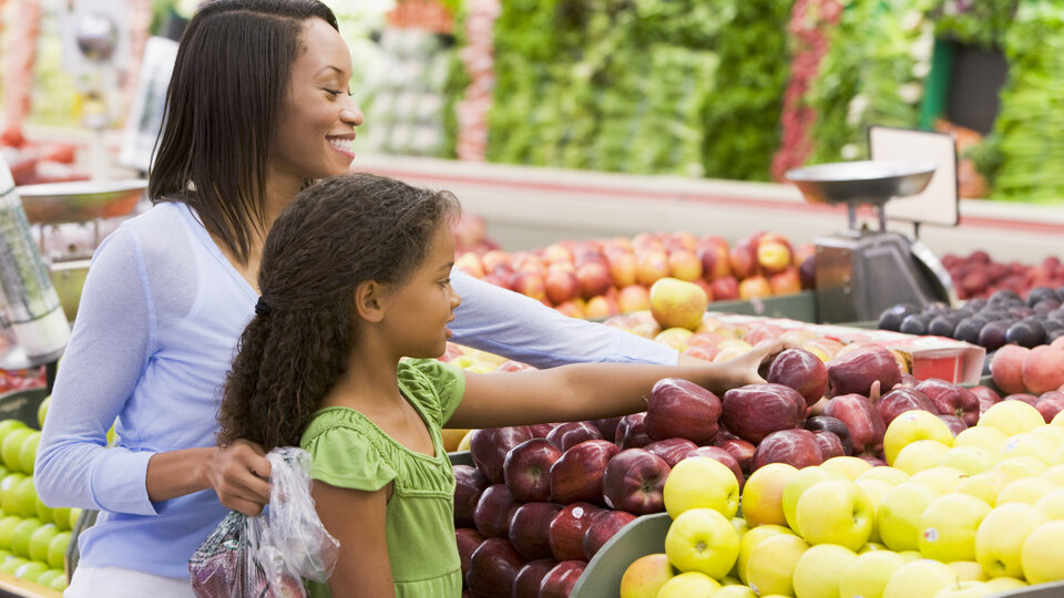 A mother helps her daughter choose produce.