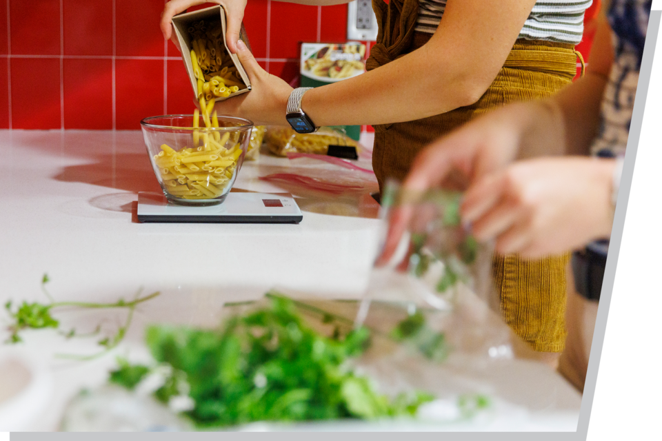 A closeup view of two girls pouring pasta and green vegetables into bowls.