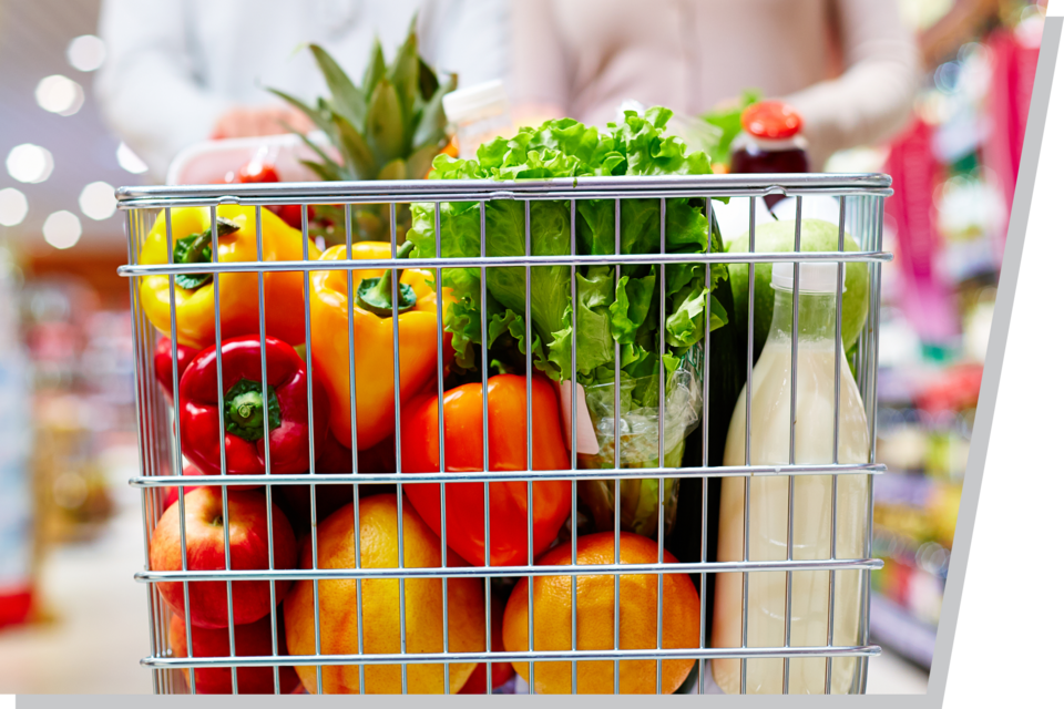 A shopping cart filled with fresh vegetables, fruit and milk.