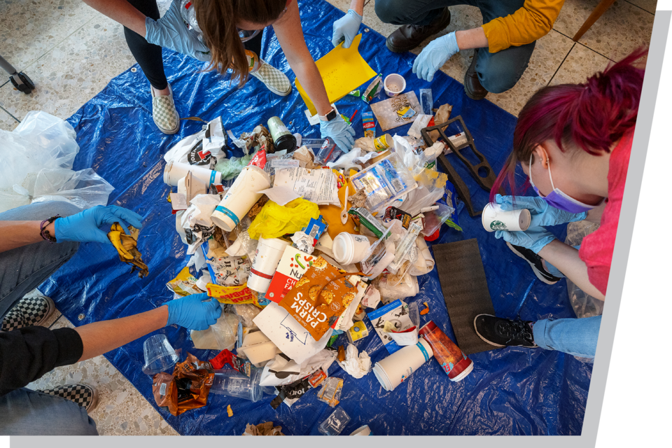 People sorting mixed trash and recyclables on a blue tarp.